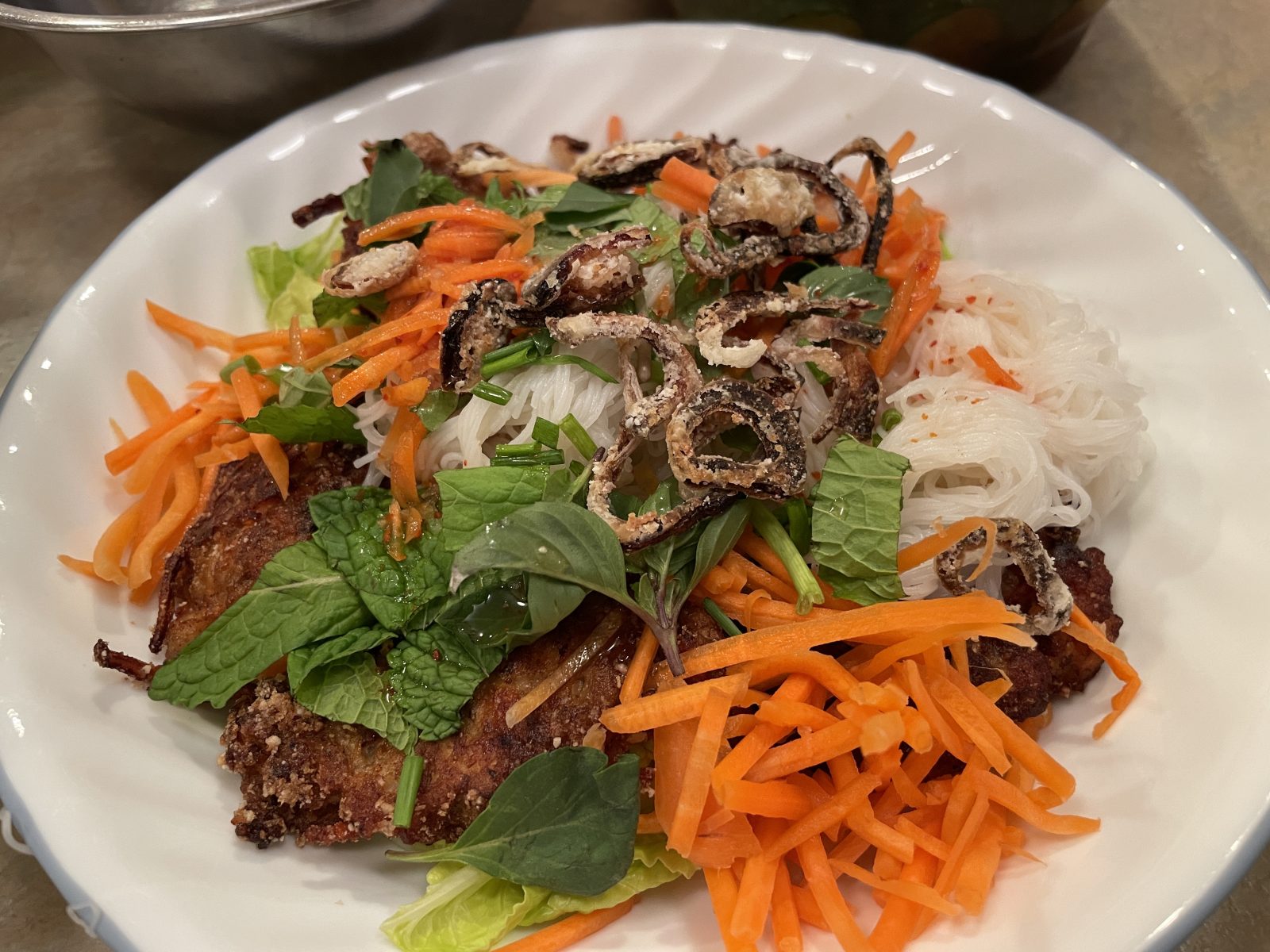 This is an assembled chicken bun cha bowl. Vermicelli rice noodles, greens, chicken patties, carrots, fresh spices and fried shallots